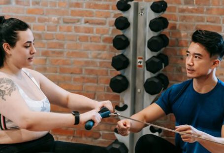 Exercise Motivation - Multiethnic trainer and overweight woman doing exercises with rowing machine together in sport club