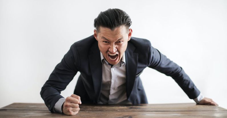 Managing Anxiety - Expressive angry businessman in formal suit looking at camera and screaming with madness while hitting desk with fist