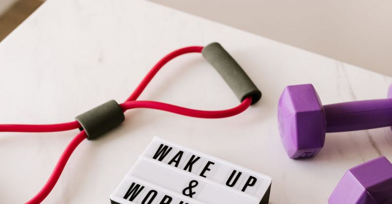 Healthy Weight - From above composition of dumbbells and massage double ball and tape and tubular expanders surrounding light box with wake up and workout words placed on white surface of table