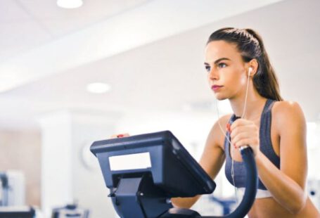 Weight Loss Goals - Serious fit woman in earphones and activewear listening to music and running on treadmill in light contemporary sports center