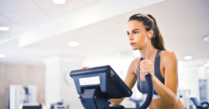 Weight Loss Goals - Serious fit woman in earphones and activewear listening to music and running on treadmill in light contemporary sports center